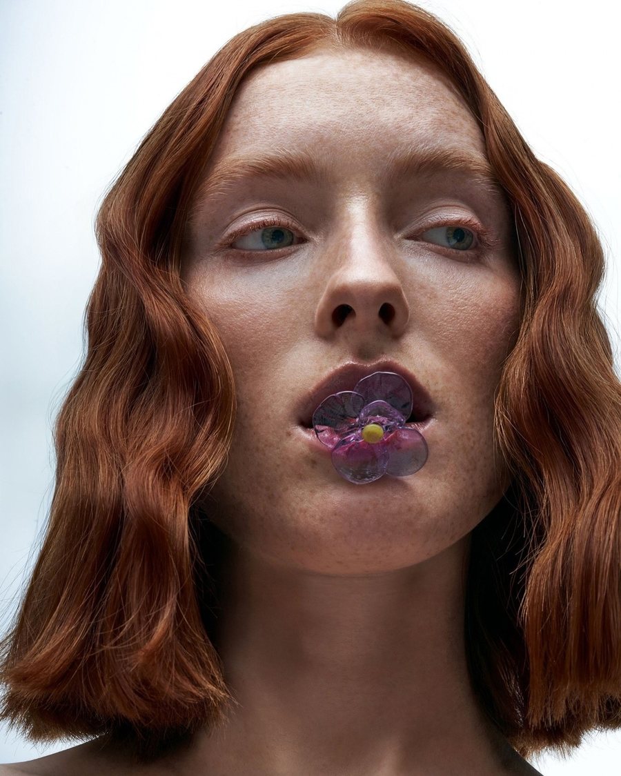 Creative beauty look: a glass flower on the lips, red hair, clear skin
